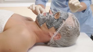 Yakışıklı erkekler yüz maskesi alma için spa terapisi. 4 k. ağır çekim. Bir güzellik uzmanı alımı