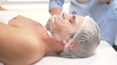 Yakışıklı erkekler yüz maskesi alma için spa terapisi. 4 k. ağır çekim. Bir güzellik uzmanı alımı