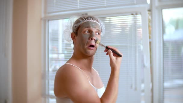Dziwny człowiek z twarzy pack. Młody człowiek robi zabiegi kosmetyczne na twarz w domu przed lustrem. 4k — Wideo stockowe