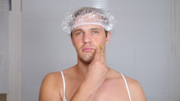 Um homem estranho com cara. Um jovem faz procedimentos cosméticos para o rosto de uma casa na frente de um espelho. 4k — Vídeo de Stock