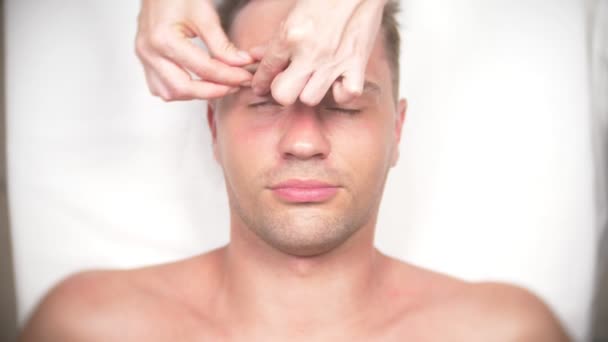 Un hombre recibiendo un masaje facial. Masajea la cara y el cuello. tumbado en la oficina del kasmetólogo. 4k, cámara lenta, vista superior — Vídeos de Stock