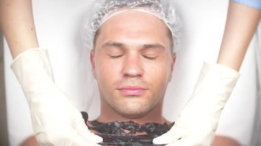 Yakışıklı erkekler yüz maskesi alma için spa terapisi. 4 k. ağır çekim. Bir güzellik uzmanı alımı