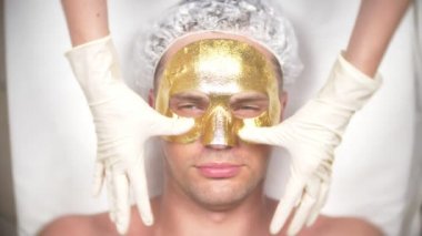Yakışıklı erkekler yüz maskesi alma için Spa terapisi. 4 k. ağır çekim. Bir güzellik uzmanı alımı. altın maske