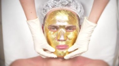 Yakışıklı erkekler yüz maskesi alma için Spa terapisi. 4 k. ağır çekim. Bir güzellik uzmanı alımı. altın maske