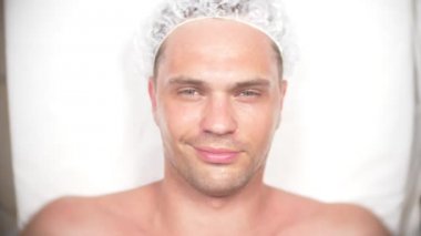 Yakışıklı erkekler yüz maskesi alma için Spa terapisi. 4 k. ağır çekim. Bir güzellik uzmanı alımı. adam kameraya gülümseyen ve göz kırpıyor arıyor.