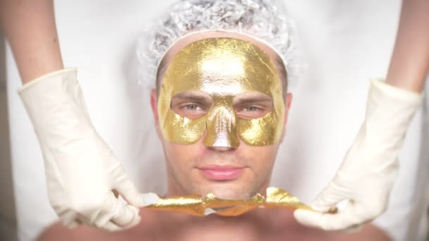 Terapia de spa para hombres guapos que reciben máscara facial. 4k. En cámara lenta. Recepción de un cosmetólogo. máscara de oro — Vídeo de stock