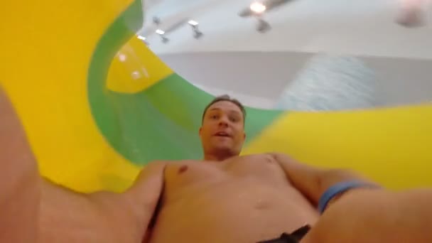 El hombre desciende del tobogán acuático a la piscina en el parque acuático. dentro de la tubería. 4k — Vídeo de stock