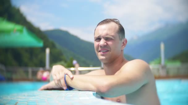 Lento movimento, fecho, reboque. jovem banho de sol e relaxar em um dia ensolarado em uma piscina de luxo em um fundo de uma paisagem montesa. resort de montanha com piscina exterior. 4k — Vídeo de Stock