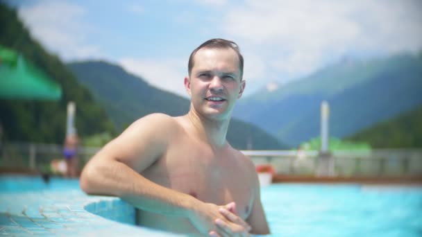 慢动作, 关闭, 肖像。年轻人在一个阳光明媚的日子里晒日光浴, 在一个高山景观的背景下, 在一个豪华的游泳池里放松。带室外游泳池的山度假村。4k — 图库视频影像