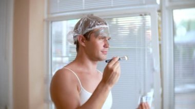 Yüz paketi olan garip adam. Genç bir adam bir ev bir ayna önünde yüz için kozmetik işlemler yapar. 4k