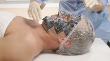 Yakışıklı erkekler yüz maskesi alma için spa terapisi. 4 k. ağır çekim. Bir güzellik uzmanı alımı