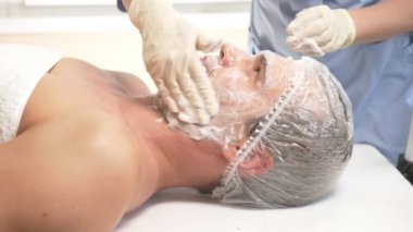 Yakışıklı erkekler yüz maskesi alma için spa terapisi. 4 k. ağır çekim. Bir güzellik uzmanı alımı