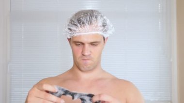 Yüz paketi olan garip adam. Genç bir adam bir ev bir ayna önünde yüz için kozmetik işlemler yapar. 4k