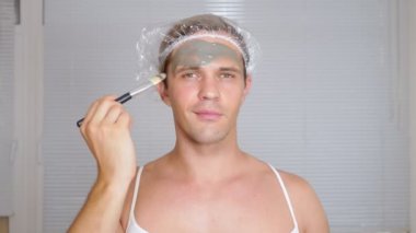 Yüz paketi olan garip adam. Genç bir adam bir ev bir ayna önünde yüz için kozmetik işlemler yapar. 4k