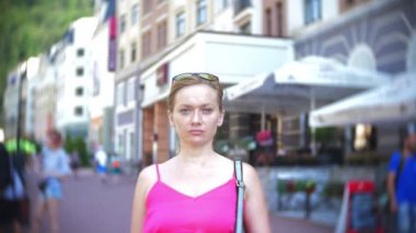 genç şık kadın, şehrin sokaklarında üzerinde poz. sıcak yaz gününde. Kamera ve gülümsüyor görünüyor. 4 k, yavaş hareket, yakın çekim.