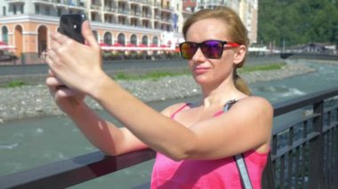 Sıcak güneşli bir günde şehirde yürüyüş smartphone kullanan kadın. Seyahat. Bir yaşam biçimi kavramı. Gadget'ı modern iletişim teknolojisi. 4k, ağır çekim