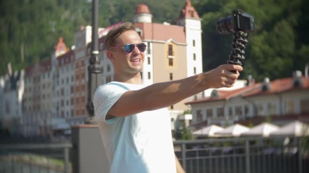 Homme, blogueur à l'aide d'une caméra, marcher dans la ville par une chaude journée ensoleillée. Voyage. Le concept d'un mode de vie. gadget des technologies de communication modernes. 4k, au ralenti — Video