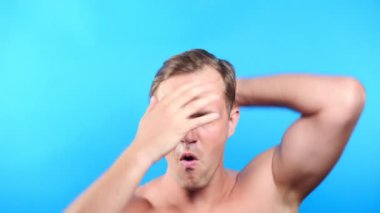Mavi renkli bir arka plan üzerinde genç adam. portre. duygu ve hareketleri. 4k, yakın çekim. Ağır çekim. adam kameraya cinsel olarak görünüyor ve dans ediyor, onun saç ayarlar