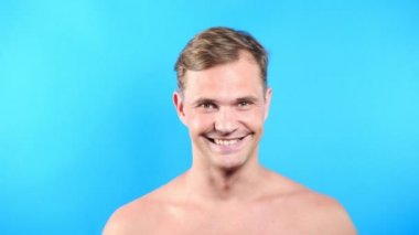 Mavi renkli arka plan üzerinde genç adam. portre. duygu ve hareketleri. 4k, yakın çekim. Ağır çekim. adam cinsel kameraya bakıyor ve onunla birlikte gitmek öneriyor.