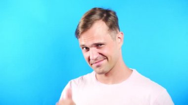 Mavi renkli arka plan üzerinde genç adam. portre. duygu ve hareketleri. 4k, yakın çekim. Ağır çekim. adam cinsel kameraya bakıyor ve onunla birlikte gitmek öneriyor.