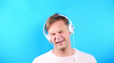 Mavi renkli bir arka plan üzerinde genç adam. portre. duygu ve hareketleri. 4k, yakın çekim. Ağır çekim. adam beyaz kulaklık müzik dinlemek