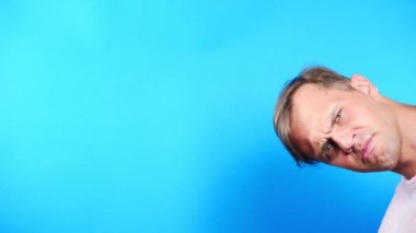 Mavi renkli bir arka plan üzerinde genç adam. portre. duygu ve hareketleri. 4k, yakın çekim. Ağır çekim. faiz ile kamera adam görünüyor. Ne olay .