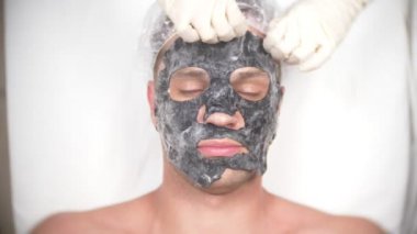 Yakışıklı erkekler yüz maskesi alma için spa terapisi. 4 k. ağır çekim. Bir güzellik uzmanı alımı
