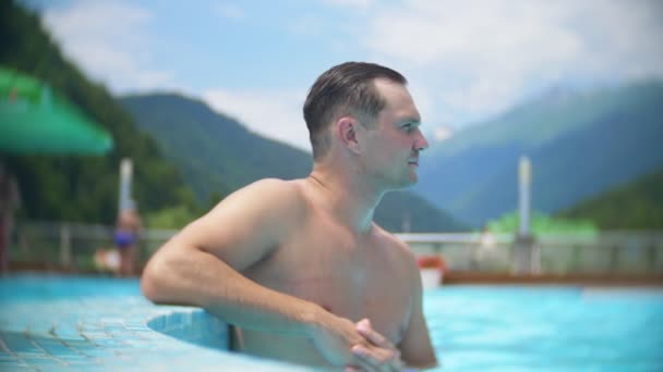 Lento movimento, fecho, reboque. jovem banho de sol e relaxar em um dia ensolarado em uma piscina de luxo em um fundo de uma paisagem montesa. resort de montanha com piscina exterior. 4k — Vídeo de Stock