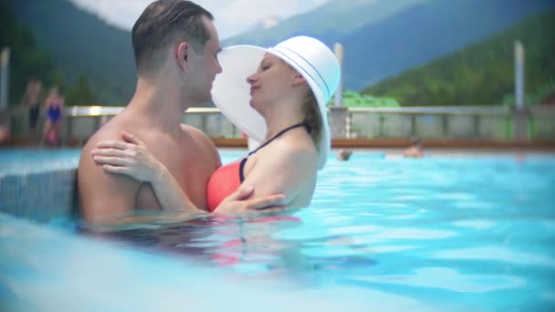 Pomalý pohyb, zavřít, portrét. šťastné milující pár muž a dívka slunění a relaxaci za slunečného dne v luxusním bazénu na pozadí horské krajiny. Mountain resort s venkovním bazénem. 4k — Stock video
