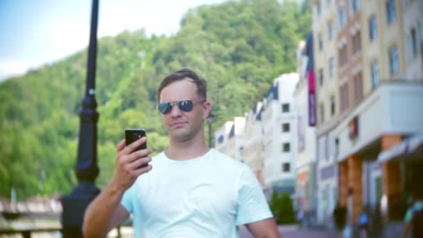 Людина використовує смартфон, що йде по місту в спекотний сонячний день. Подорожі. Поняття способу життя. гаджет сучасних комунікаційних технологій. 4k, повільний рух — стокове відео