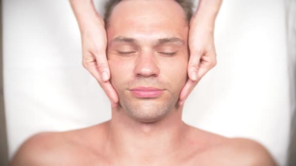 Чоловік отримує масаж обличчя. Масаж обличчя і шиї. лежав у кабінеті кастомолога. 4k, повільний рух, вид зверху — стокове відео
