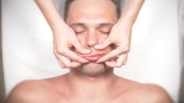 Un hombre recibiendo un masaje facial. Masajea la cara y el cuello. tumbado en la oficina del kasmetólogo. 4k, cámara lenta, vista superior — Vídeo de stock