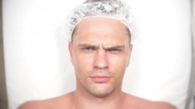 Yakışıklı erkekler yüz maskesi alma için Spa terapisi. 4 k. ağır çekim. Bir güzellik uzmanı alımı. adam kameraya gülümseyen ve göz kırpıyor arıyor.