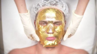 Yakışıklı erkekler yüz maskesi alma için Spa terapisi. 4 k. ağır çekim. Bir güzellik uzmanı alımı. altın maske