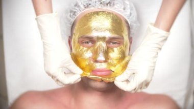Yakışıklı erkekler yüz maskesi alma için Spa terapisi. 4 k. ağır çekim. Bir güzellik uzmanı alımı. altın maske