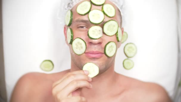 Um homem estranho com cara. Um jovem faz procedimentos cosméticos para o rosto de uma casa na frente de um espelho. 4k, máscara de pepino — Vídeo de Stock