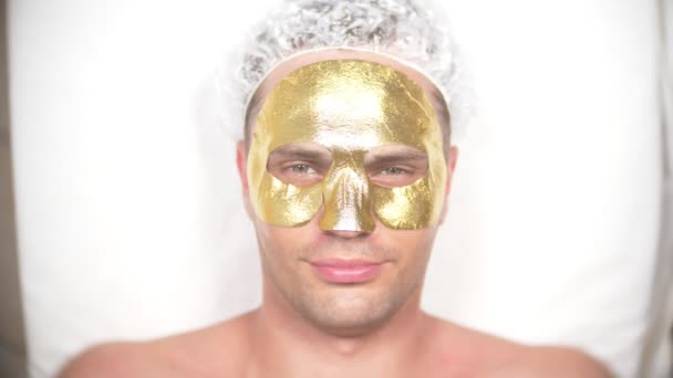 Wellnesstherapie für gut aussehende Männer mit Gesichtsmaske. 4k. Zeitlupe. Empfang eines Kosmetikers. Goldene Maske — Stockvideo