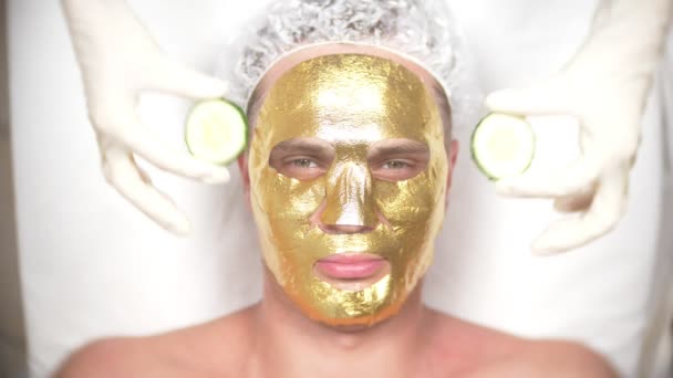 Wellnesstherapie für gut aussehende Männer mit Gesichtsmaske. 4k. Zeitlupe. Empfang eines Kosmetikers. Goldene Maske — Stockvideo