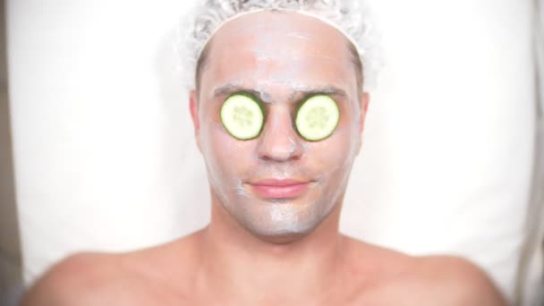 Un hombre extraño con mochila facial. Un joven hace procedimientos cosméticos para la cara de una casa frente a un espejo. 4k, máscara de pepino — Vídeo de stock