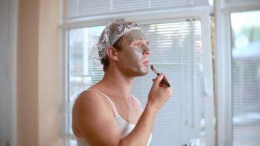 Yüz paketi olan garip adam. Genç bir adam bir ev bir ayna önünde yüz için kozmetik işlemler yapar. 4k