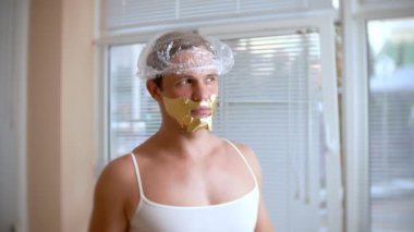 Yüz paketi olan garip adam. Genç bir adam bir ev bir ayna önünde yüz için kozmetik işlemler yapar. 4k, altın maske