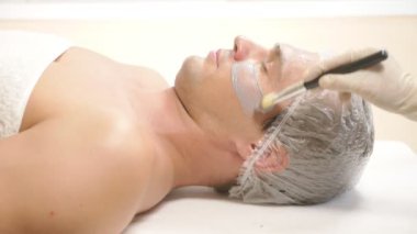 Yakışıklı erkekler yüz maskesi alma için spa terapisi. 4 k. ağır çekim. Bir güzellik uzmanı alımı