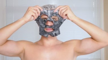 Yüz paketi olan garip adam. Genç bir adam bir ev bir ayna önünde yüz için kozmetik işlemler yapar. 4k