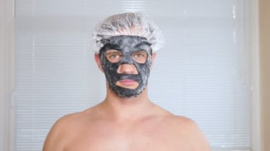 Yüz paketi olan garip adam. Genç bir adam bir ev bir ayna önünde yüz için kozmetik işlemler yapar. 4k