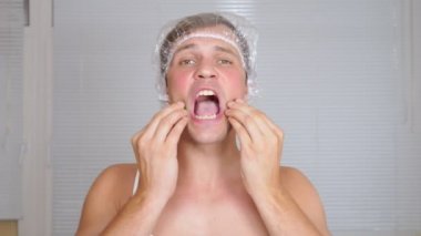 Yüz paketi olan garip adam. Genç bir adam bir ev bir ayna önünde yüz için kozmetik işlemler yapar. 4k