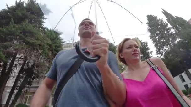 Un couple amoureux d'hommes et de femmes se promène sous un parapluie dans le parc par un jour pluvieux d'été. 4k. caméra d'action — Video