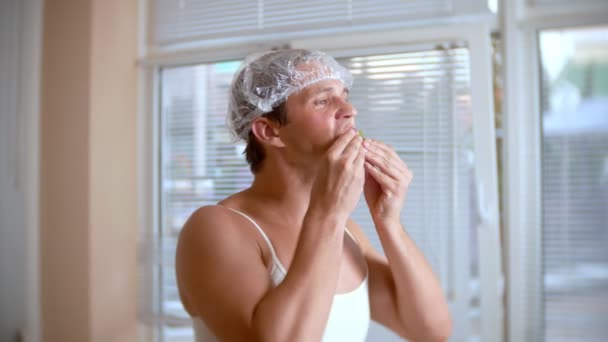 Främmande man med ansikte pack. En ung man gör kosmetiska behandlingar för ansiktet av ett hus framför en spegel. 4k — Stockvideo