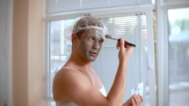 Strange man with face pack. A young man does cosmetic procedures for the face of a house in front of a mirror. 4k — Stock Video