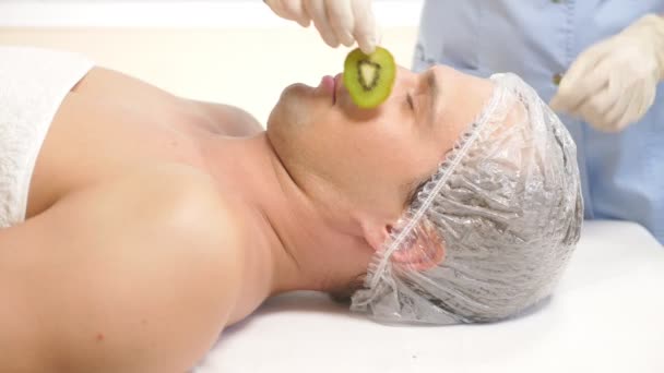 Terapia de spa para hombres guapos que reciben máscara facial. 4k. En cámara lenta. Recepción de un cosmetólogo. máscara de kiwi — Vídeo de stock