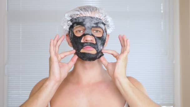 Strange man with face pack. A young man does cosmetic procedures for the face of a house in front of a mirror. 4k — Stock Video